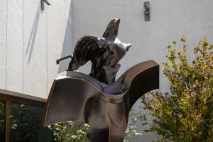 A bronze sculpture of a bird flying out of a book in a garden setting.