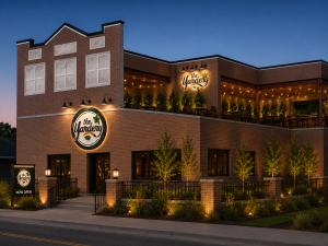 Architectural rendering of The Yardery Wildwood at dusk, showing a two-story brick restaurant with illuminated Yardery signage, a rooftop bar and dining area, outdoor gathering spaces, landscaping, and warm string lighting. The venue is scheduled to open