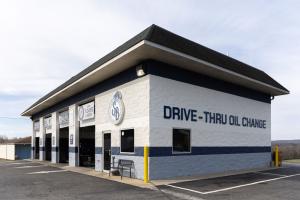 Exterior of a Strickland Brothers drive-thru oil change location, featuring a white-and-blue building with multiple drive-thru service bays, branded signage, and a parking area in front.