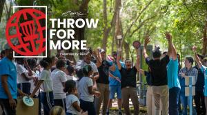 Throw For More graphic over a photo of disc golfers and community members celebrating on a disc golf course.