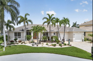 Front exterior of a 2,368-square-foot home for sale in Punta Gorda featuring three bedrooms, three baths, mature palm trees, tropical landscaping and a circular driveway on a 0.23-acre homesite.