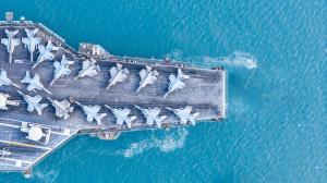 A nuclear-powered aircraft carrier with parked fixed-wing aircraft on its flight deck, surrounded by blue water.