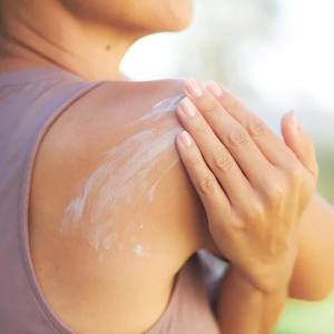 A woman rubbing lotion on her shoulder.