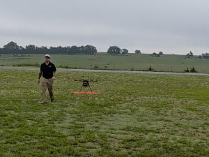 Vigilant Aerospace Director of Operations Kendyn Webster walking away from a drone sitting in a grassy field behind him.