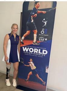 Kendra Herber, World No. 1 para standing tennis player and moorlow partner, standing next to the World Championships banner at Monviso Tennis Club in Turin, Italy.