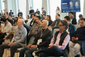 A seated audience watching a presentation in a modern conference room, with a Fireside slide visible on screen in the background.