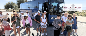 Group of tourists standing near a blue tour bus in a sunny desert area with Indian Wells, California sign in the background.