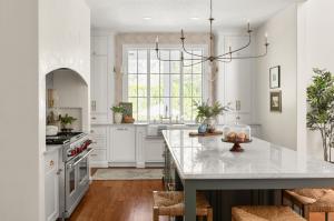 Remodeled DeLand, FL kitchen by KBF Design Gallery with a large window over a farmhouse sink, brass bridge faucet, Quartzitze countertops, green island, and a stainless Wolf range beneath an arched niche.