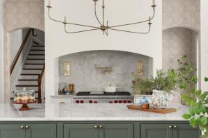 Award-winning DeLand, FL kitchen by KBF Design Gallery featuring a stainless Wolf range set in an arched niche, a quartzite slab backsplash with a brass pot filler, and a green island with a marble-look countertop.