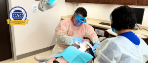 Dentist and assistant wearing protective gear treating a patient in a dental clinic with Certified Autism Center logo visible.