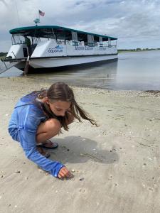 Girl on beach looking for shells, with the Tour Boat in background