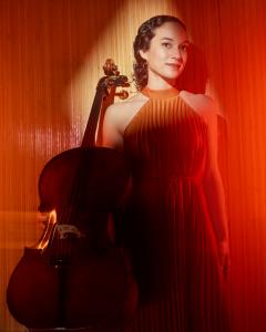 Francesca is a black woman wearing an orange dress, holding her cello