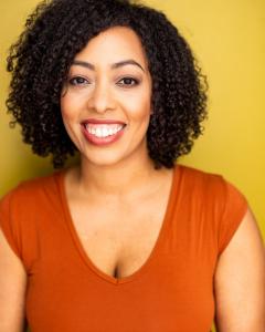Lyndsay is a black woman with curly hair and tattoos wearing an orange shirt