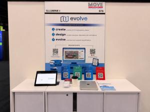 EVOLVE booth at the MOVE America event with a banner and demo on a monitor. Brochures and QR code scanners on the desk.