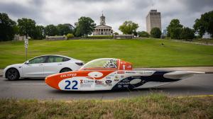 University of Illinois solar car Calypso, No. 22, driving on a public road past the Tennessee State Capitol with a white Tesla alongside.