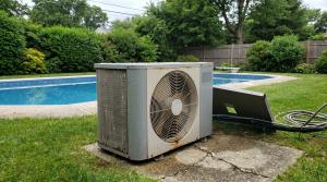 Weathered pool heat pump unit beside an inground pool in a Bellport, Long Island backyard awaiting service