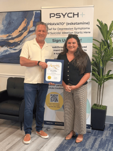 Chris Cox stands with a representative from the California State Assembly in front of a PsychPlus banner, holding a Certificate of Recognition during the Riverside clinic grand opening.