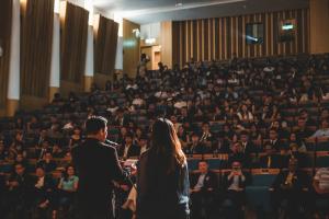 Two people stood up facing the audience at an awards ceremony. The man on the left is reading from a piece of paper