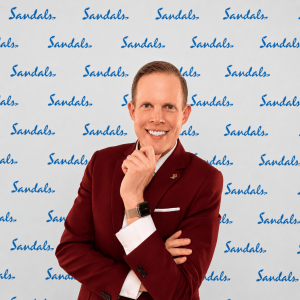 Photo of Addison Jaynes, the founder and CEO of Reliant Destinations at the Sandals STAR Awards in front of a Sandals-logo backdrop.