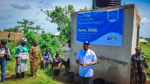 Representative from Hope Spring Water stands beside a child at the completed Ido-Osun Community Borehole Project in Osun State, Nigeria, celebrating improved access to safe drinking water.