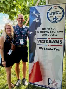 Jeff Nydegger, owner of veteran-owned Jeff Buys Your House, and his wife, Sarah, stand beside a Rockin' for Our Vets sponsor sign at Cantigny Park, where the company supports programs benefiting veterans.