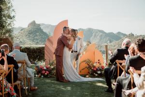 Groom kisses his bride at their San Diego wedding ceremony while guests clap and cheer.