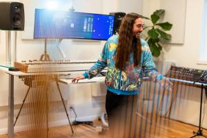 Luke F. Walton in a recording studio, in front of a musical and computer keyboard, gesturing to his collaborator off-screen