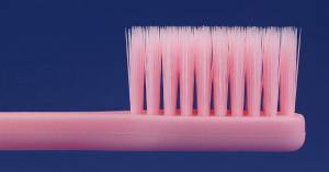 Close-up of soft toothbrush bristles on a pink toothbrush against a navy background.