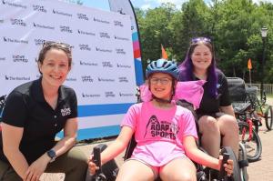 Three people pose in front of a banner with adaptive sports equipment
