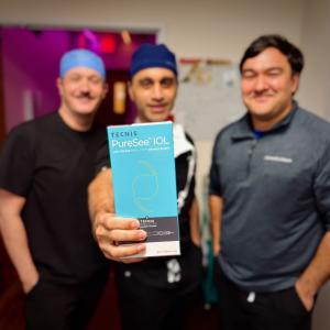 Dr. Sobti, dressed in surgical cap and scrubs, poses with the Johnson & Johnson ophthalmic team and displays the box of the new TECNIS PureSee IOL