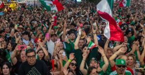 A packed crowd of thousands of fans wearing Mexico soccer jerseys waves Mexican flags and cheers during Adriana's Puro Soccer Fest in Downtown Chula Vista, celebrating the FIFA World Cup with music, culture, and community.