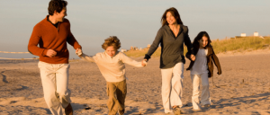 Family of four joyfully running and holding hands on a sandy beach during sunset.