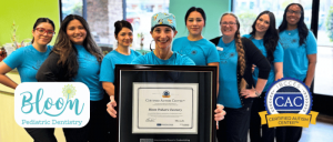 Group of eight smiling dental staff in blue shirts with a certificate for Bloom Pediatric Dentistry as a Certified Autism Center.