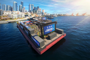 The Seattle Soccier Celebration fan zone with mini soccer field, fans, and screens floating in Elliot Bay.