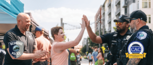 A woman high-fiving two Redmond police officers during a community event on a sunny day with people in the background.