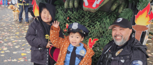 Police officer kneeling next to a smiling boy wearing a Deadpool hat and a Los Angeles baseball jersey at an outdoor event.