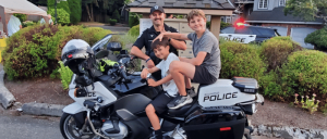 Two children sit on a Redmond Police motorcycle with a police officer standing behind them in a residential neighborhood.