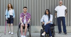 photo of four models of varying genders, ages, disabilities and ethnicities posing towards the camera. the two inner models are seated in wheelchairs while the outer two models are standing.