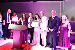 Farrah Mechael stands on stage holding her Ambassador for Peace certificate with Universal Peace Federation representatives and event organizers during the inaugural Peace Gala.