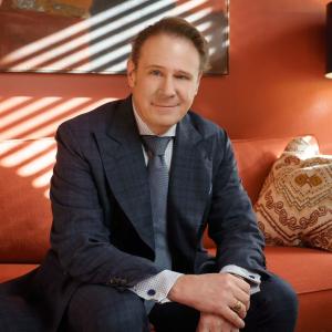 Professional portrait of Chris Small, founder of Park 27 Group and Richmond REALTOR®, seated in a modern interior wearing a navy suit and tie.