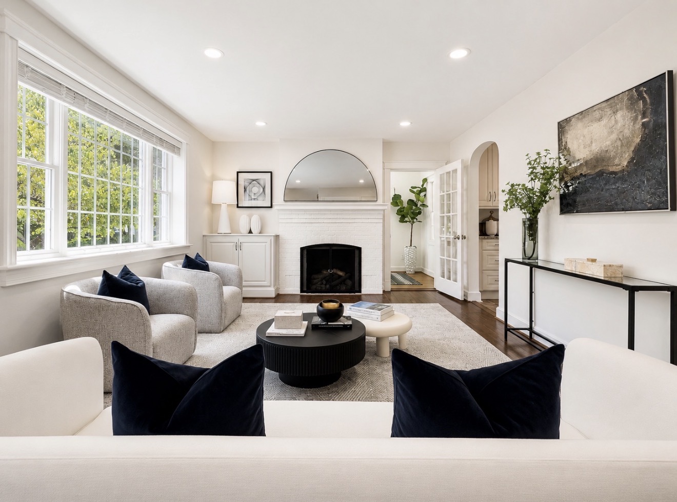 Professionally staged contemporary living room with white seating, black coffee table, designer artwork, and neutral finishes.