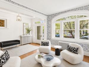 Historic living room with a large arched window, blue patterned wallpaper, white boucle chairs, modern coffee table, and professionally staged furnishings.