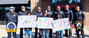 Group of police officers standing behind children holding colorful autism awareness signs, with Certified Autism Center and Merced Police logos.