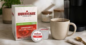A box and individual pods of Hurricane Coffee and Tea's Category 5 commercially compostable coffee, shown next to a brewed pot of coffee and a Keurig-compatible brewing machine.