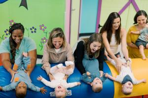 Parents and babies laughing together on colorful gym mats during a Romp n' Roll baby class at Babypalooza