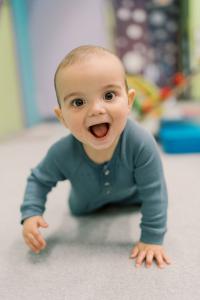 Excited baby boy crawling on the floor with a big smile during Romp n' Roll's Babypalooza event