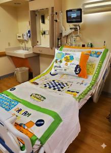 A child's hospital bed outfitted with blue Playtime Edventures interactive therapy sheets featuring over 65 vibrant board games, educational activities, and a central gold star layout designed to reduce pediatric anxiety.