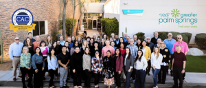 Group photo of diverse adults standing outdoors in front of a building with "Certified Autism Center" and "Visit Greater Palm Springs" logos.