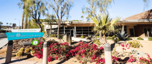 Visitors Center building in Greater Palm Springs surrounded by desert plants and vibrant flowering bushes under a clear sky.