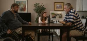 Tobias Forrest, a man in a wheelchair, child actor Victoria Scott and double-hand amputee John W. Lawson sit around a table in a tense scene from DARUMA.
